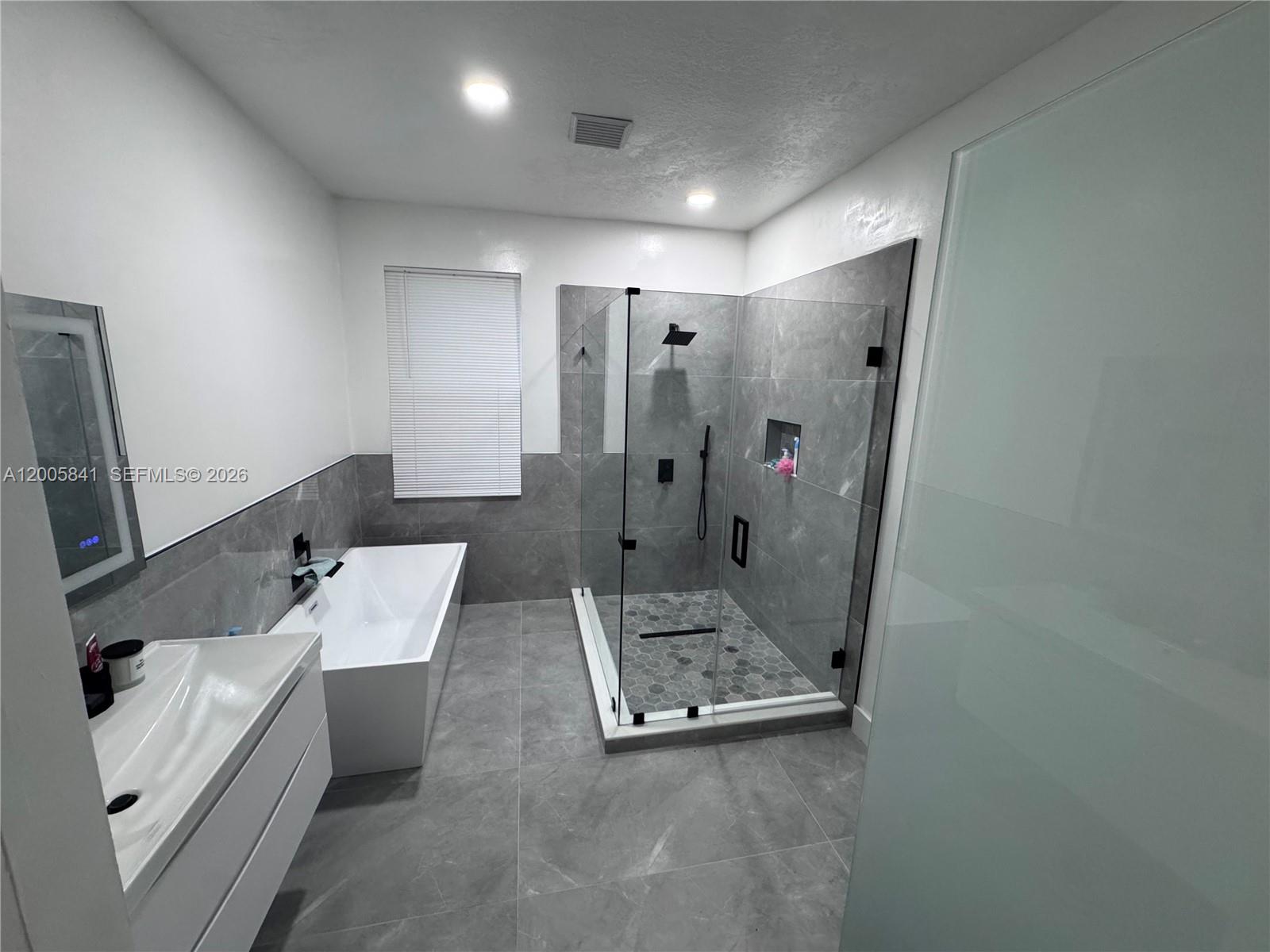A modern bathroom features a freestanding tub, a glass-enclosed shower, and gray tile flooring — 23922 SW 108th Ave, Homestead FL 33032, HOMESTEAD, FL