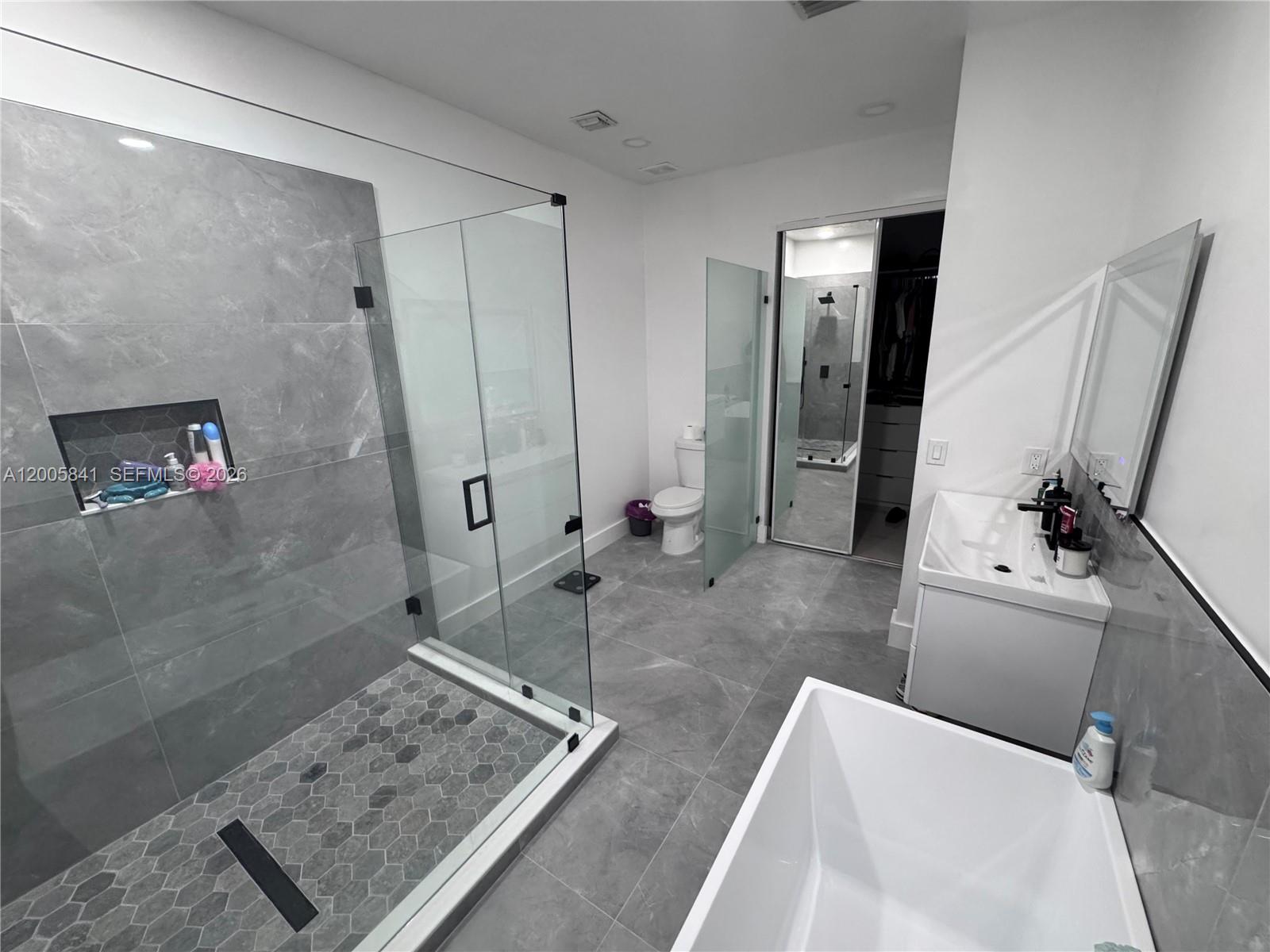 A modern bathroom features a glass-enclosed shower, a freestanding tub, and gray tile flooring — 23922 SW 108th Ave, Homestead FL 33032, HOMESTEAD, FL