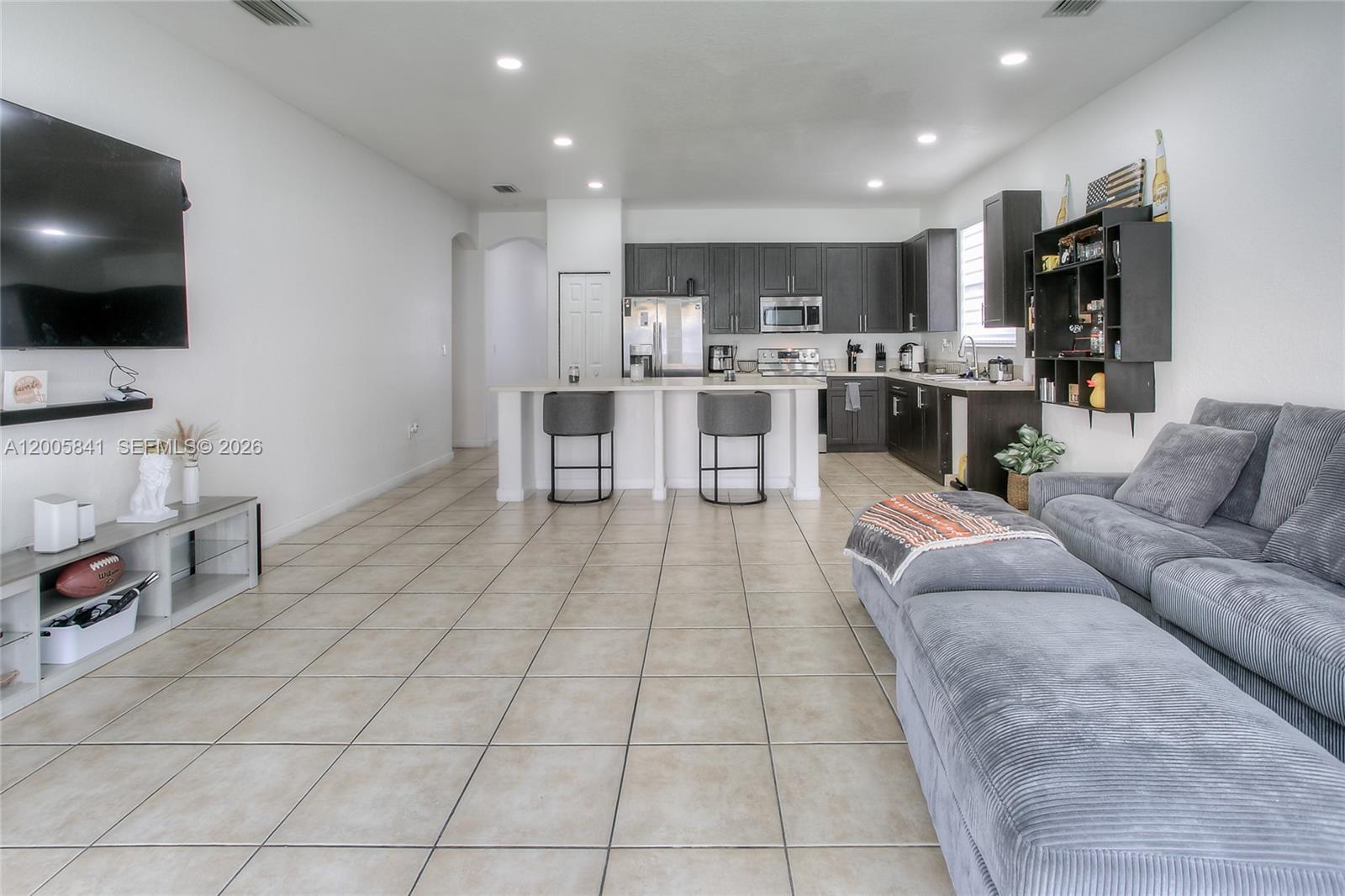 An open-concept living room and kitchen featuring tile floors, dark cabinetry, and a grey sectional — 23922 SW 108th Ave, Homestead FL 33032, HOMESTEAD, FL