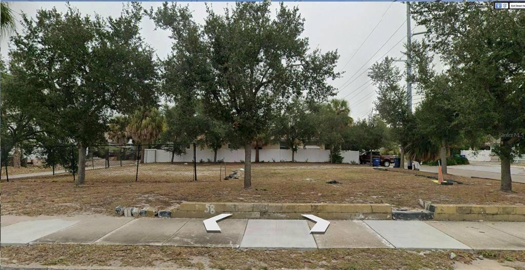 A vacant, grassy residential lot features a low retaining wall and several mature trees — 1101 N HOWARD AVENUE, TAMPA, FL