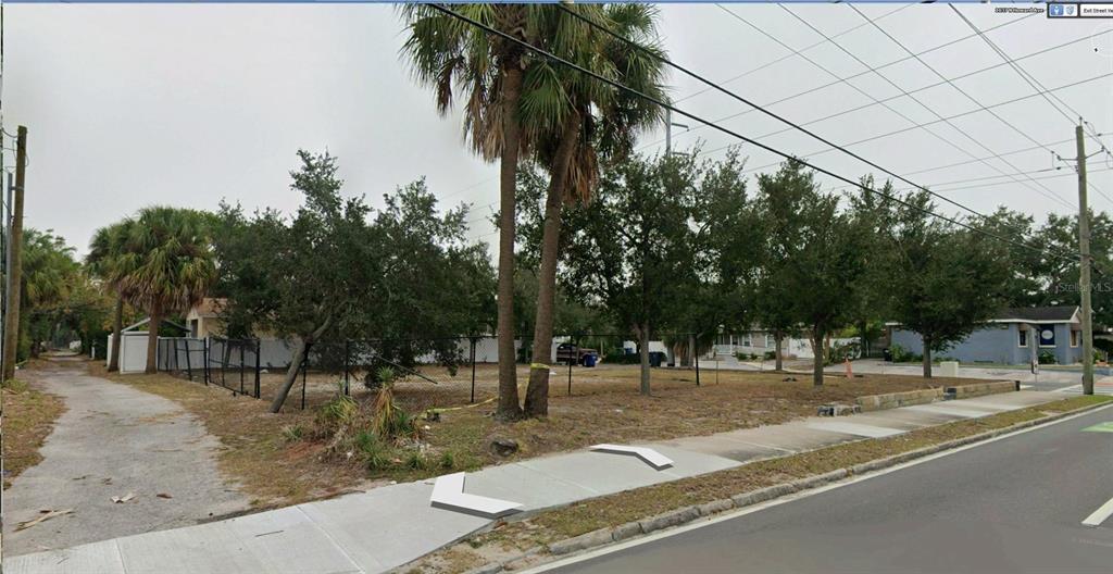 A vacant, fenced-in lot with several trees sits next to a paved driveway and sidewalk — 1101 N HOWARD AVENUE, TAMPA, FL