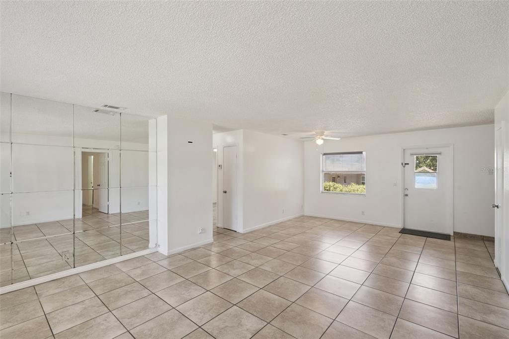 A bright living room features large beige floor tiles, white walls, and a mirrored wall — 4225 NE 25TH AVENUE, OCALA, FL