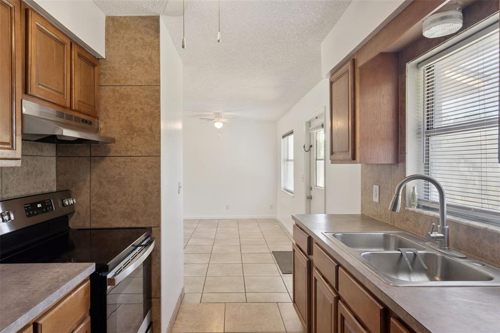 A galley kitchen with wood cabinets, tile backsplash, and stainless steel appliances leads to a dining area — 4225 NE 25TH AVENUE, OCALA, FL