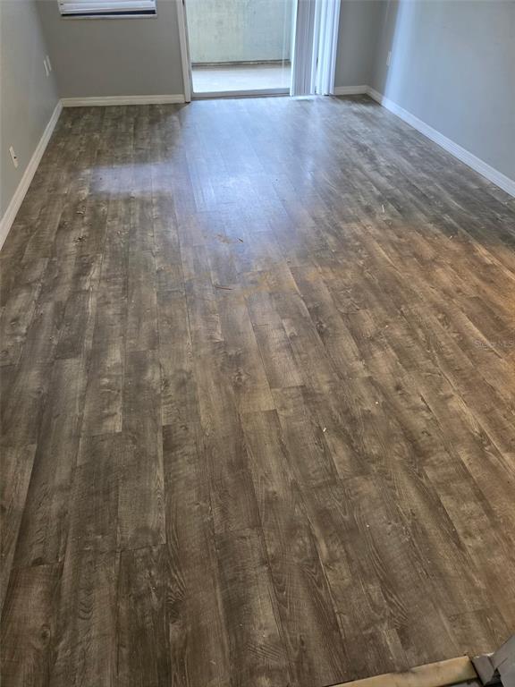 An empty room with gray wood-look flooring and a sliding glass door leading to a balcony — 2939 LOS ALTOS DRIVE UNIT B, BELLEAIR BLUFFS, FL