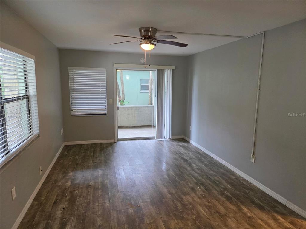 An empty room features gray walls, wood-look flooring, a ceiling fan, and a sliding glass door — 2939 LOS ALTOS DRIVE UNIT B, BELLEAIR BLUFFS, FL