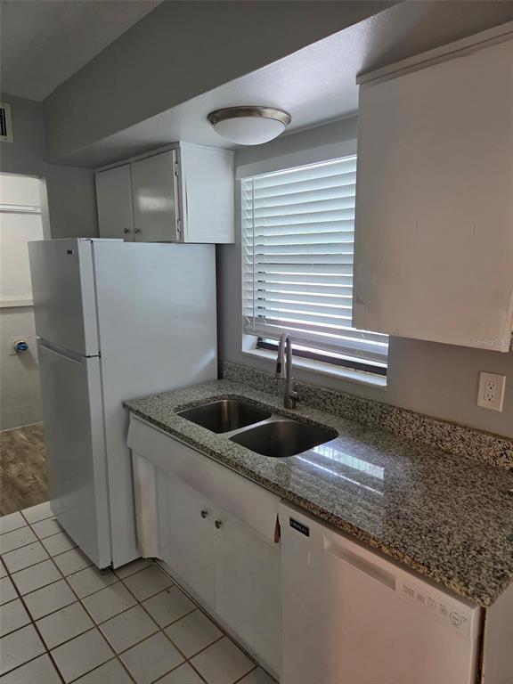 A kitchen featuring white cabinets, granite countertops, a stainless steel sink, and white appliances — 2939 LOS ALTOS DRIVE UNIT B, BELLEAIR BLUFFS, FL
