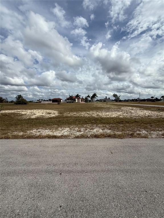 A vacant, grassy residential lot sits along a paved road under a cloudy sky — 2801 NW 45TH PLACE, CAPE CORAL, FL