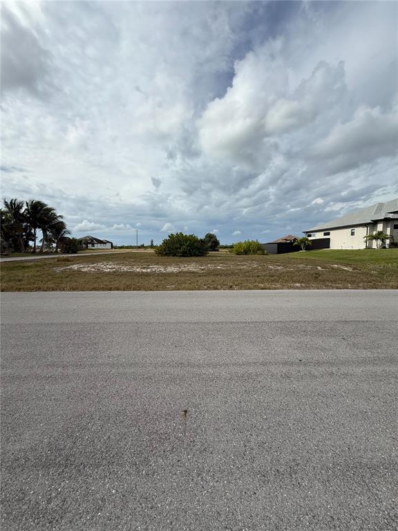 A vacant, grassy residential lot sits along a paved road under a cloudy sky — 2801 NW 45TH PLACE, CAPE CORAL, FL