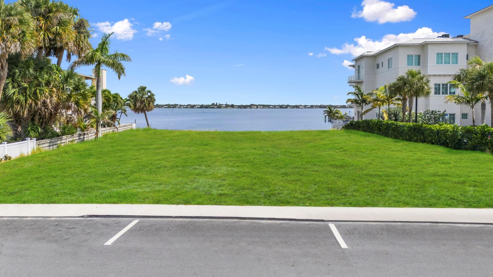 A vacant grassy waterfront lot sits between two buildings under a clear blue sky — 39 SE Seminole Street, Stuart FL 34994, STUART, FL