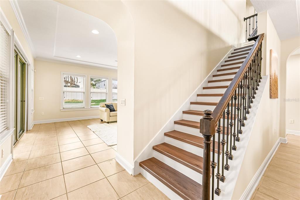 A staircase with dark wood treads and metal railings stands beside a tiled living area — 14252 CREEKBED CIRCLE, WINTER GARDEN, FL