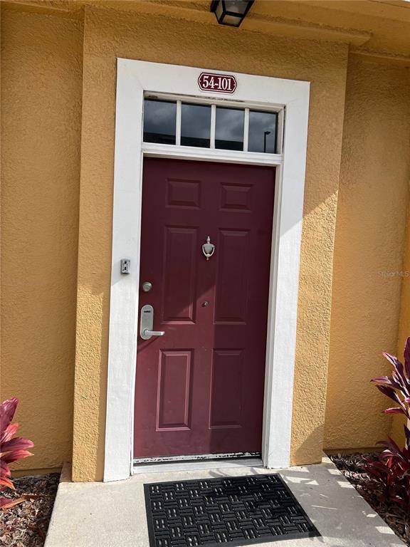 A maroon front door with a transom window is set in a yellow stucco wall — 4010 SANTA MARIA DRIVE UNIT 101, KISSIMMEE, FL