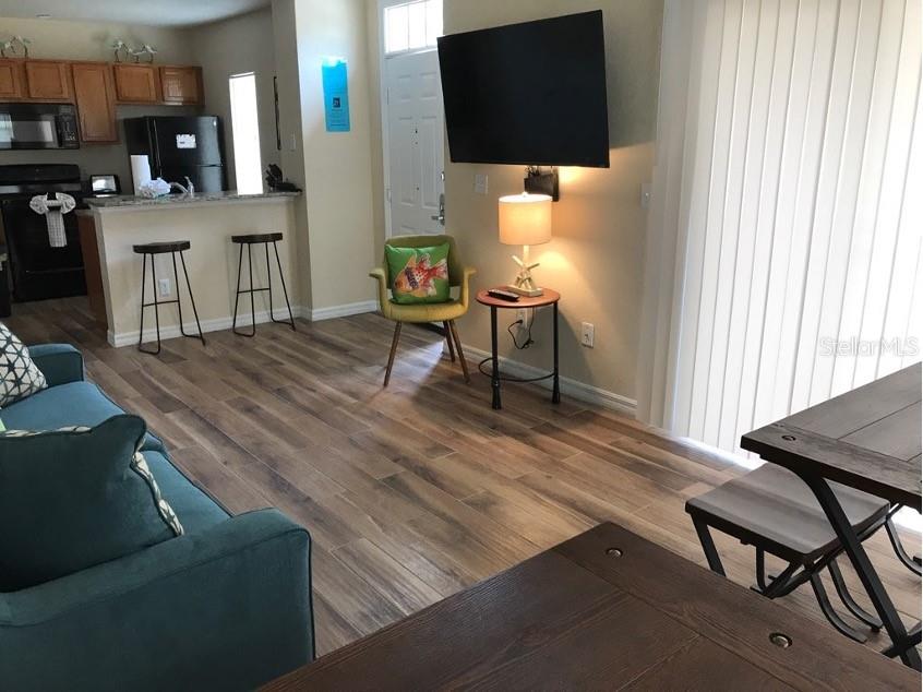 A living room with wood-look tile floors, a teal sofa, and an open kitchen area — 4010 SANTA MARIA DRIVE UNIT 101, KISSIMMEE, FL