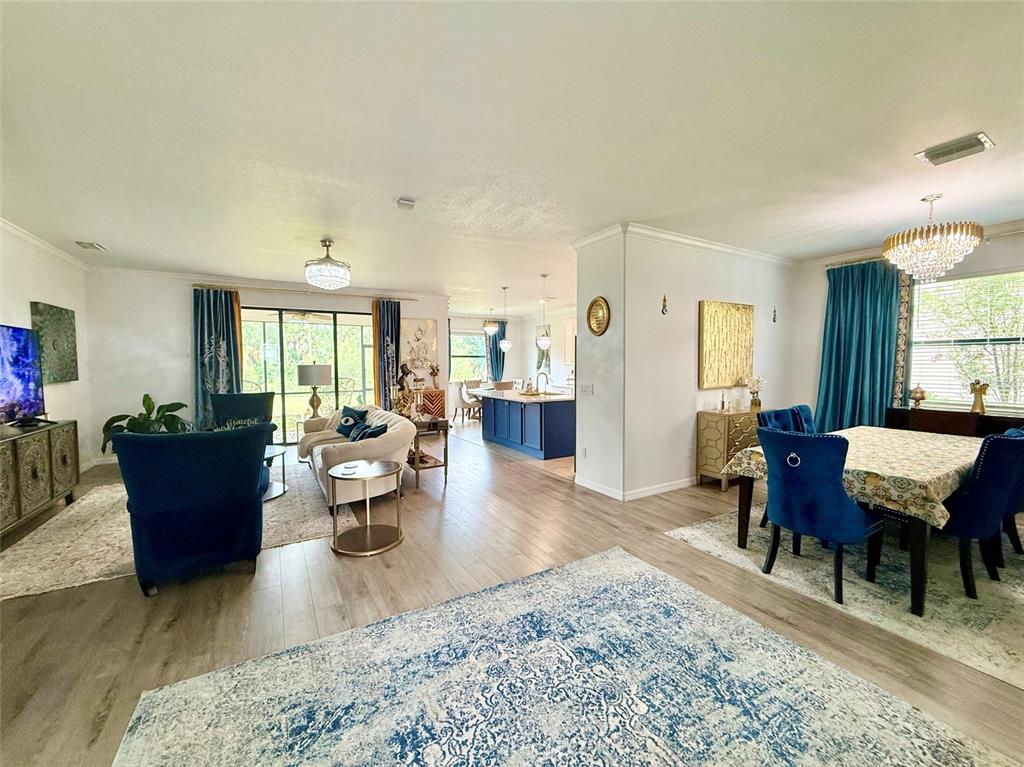 An open-concept living and dining area features blue velvet furniture, light wood flooring, and chandeliers — 20642 BENISSIMO DRIVE, VENICE, FL