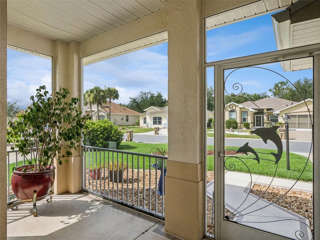 A screened-in porch features a potted plant, metal railing, and a decorative dolphin-themed screen door — 4519 INVERNESS DRIVE, LEESBURG, FL