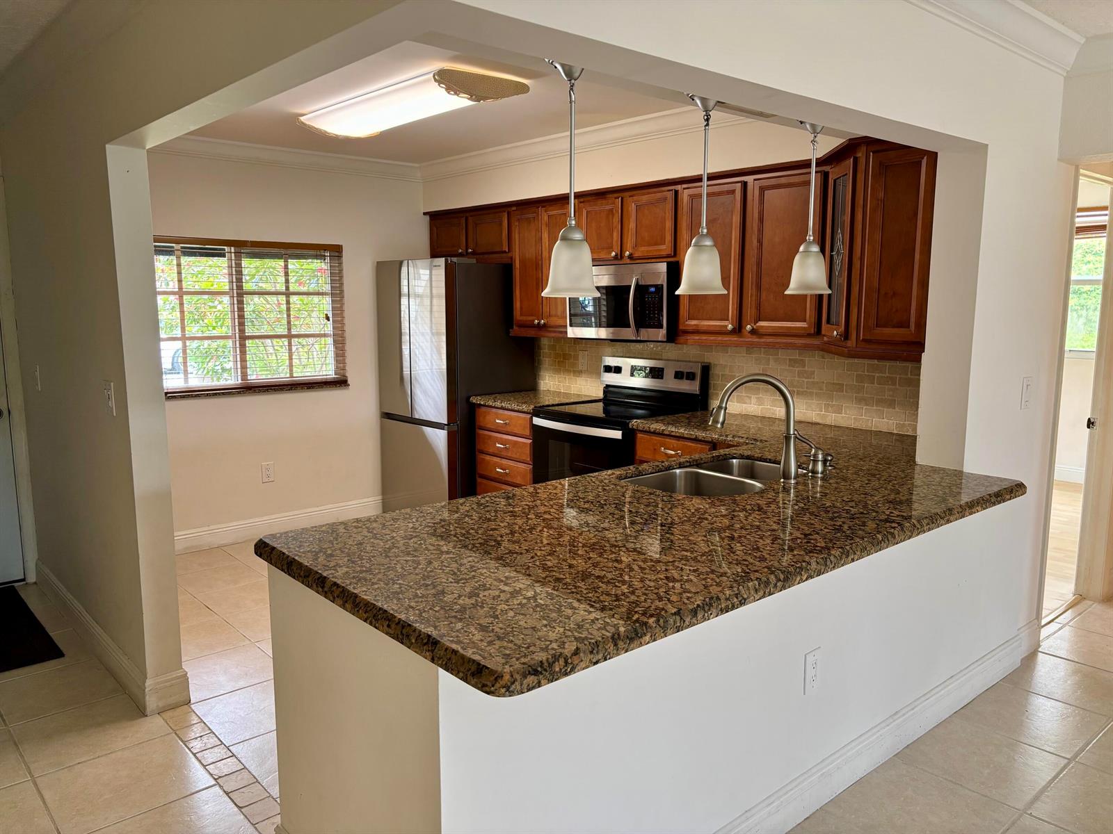 A kitchen with wood cabinets, granite countertops, stainless steel appliances, and a breakfast bar — 4040 Crystal Lake Drive # 101, Pompano Beach FL 33064, POMPANO BEACH, FL