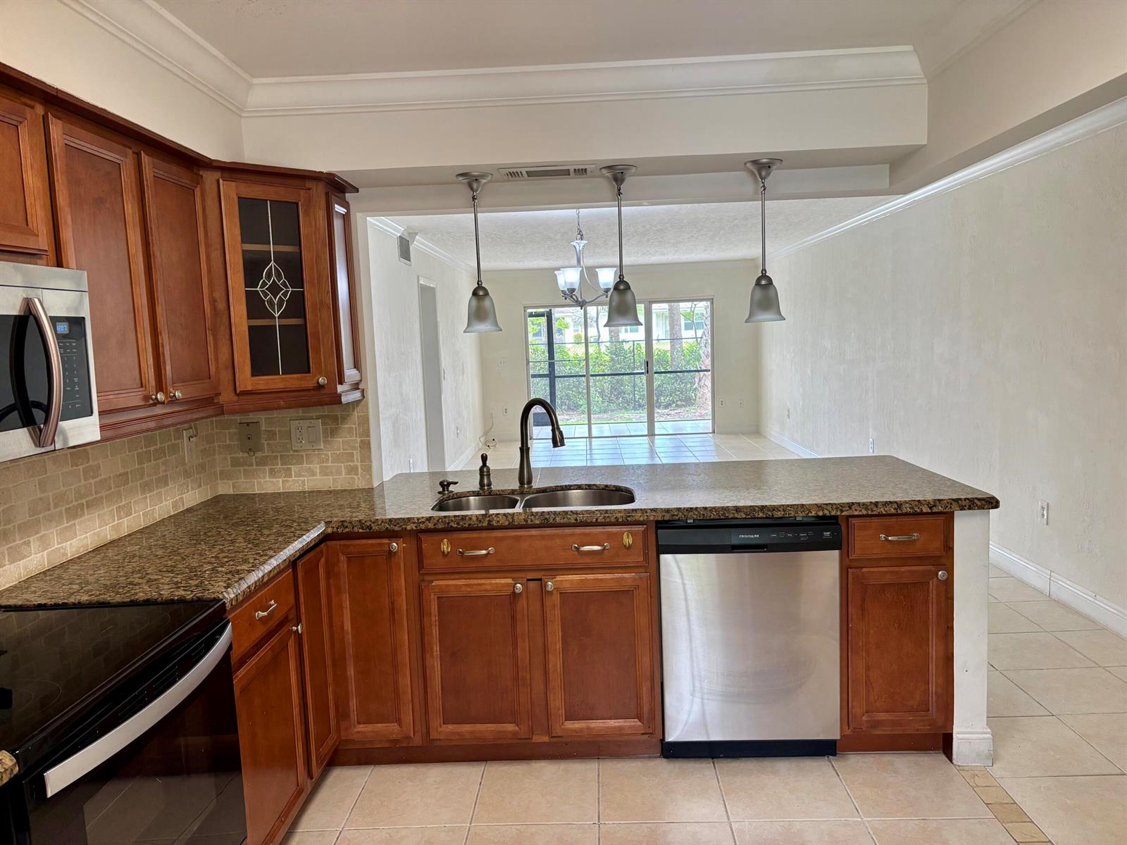 A kitchen with wood cabinets, granite countertops, and stainless steel appliances overlooks a living area — 4040 Crystal Lake Drive # 101, Pompano Beach FL 33064, POMPANO BEACH, FL