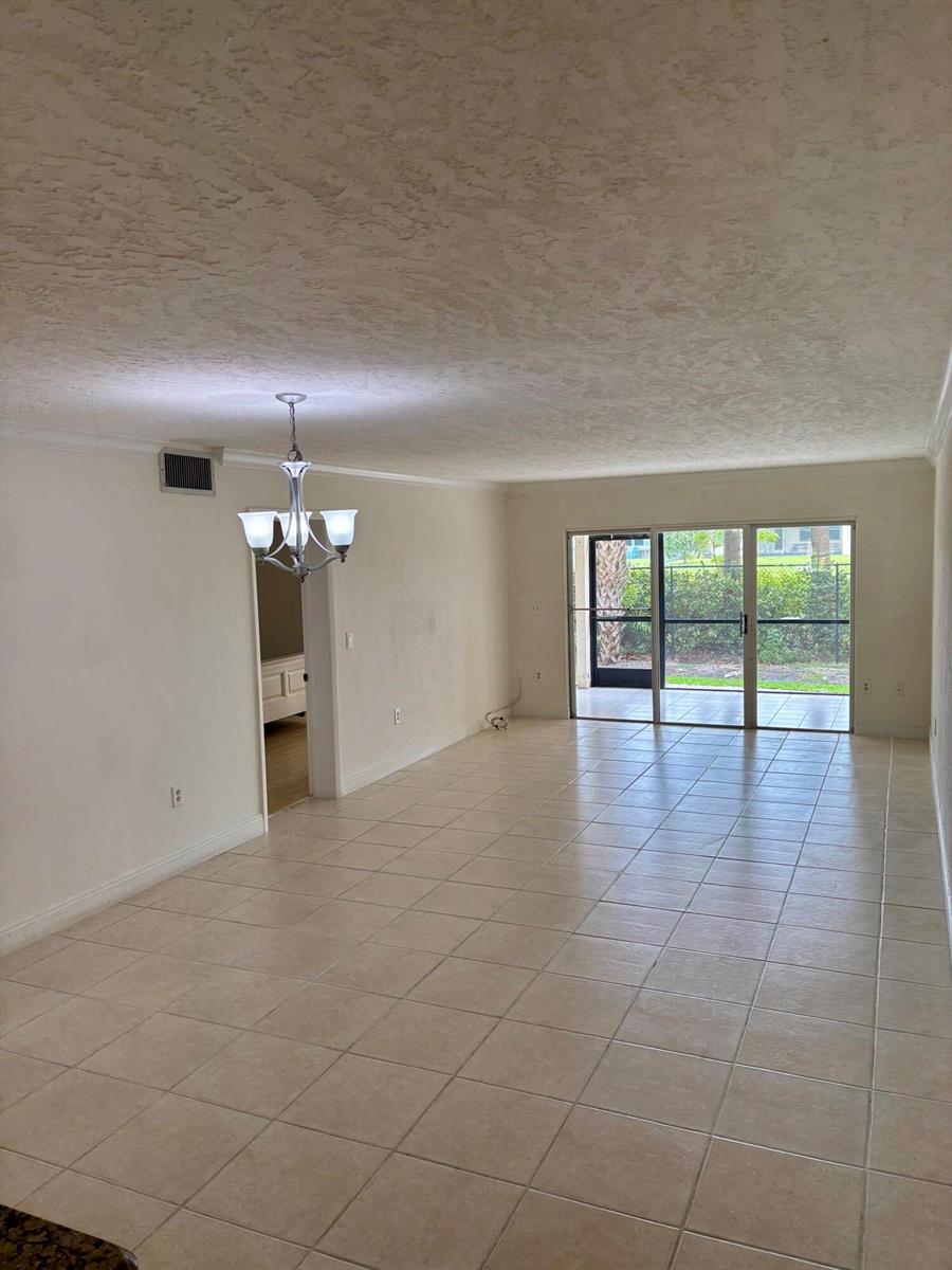 An open living area features light-colored tile flooring, a chandelier, and sliding glass patio doors — 4040 Crystal Lake Drive # 101, Pompano Beach FL 33064, POMPANO BEACH, FL