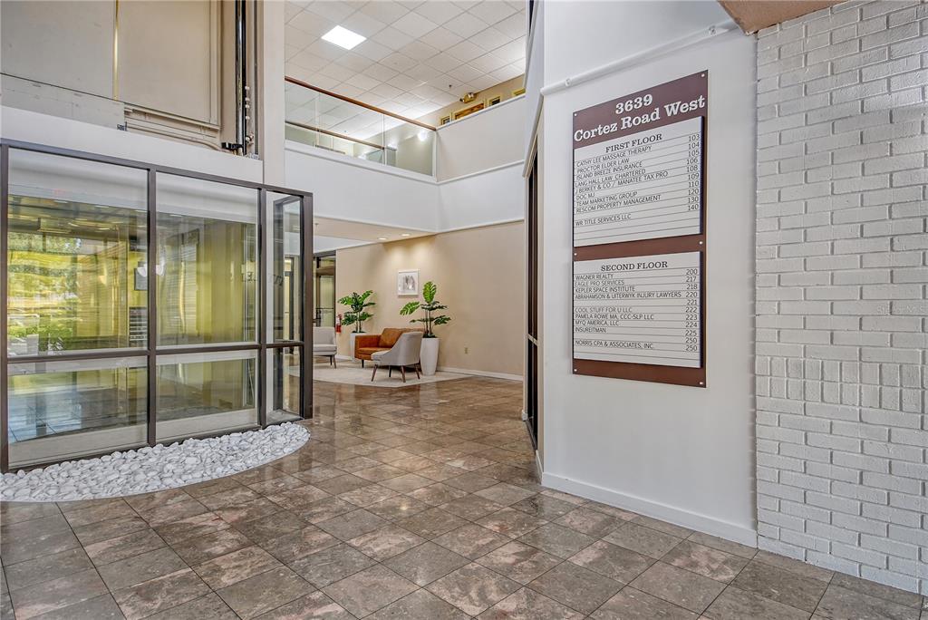 A commercial building lobby features a directory sign, tiled floors, and a glass-enclosed elevator — 3639 CORTEZ ROAD W UNIT 225, BRADENTON, FL