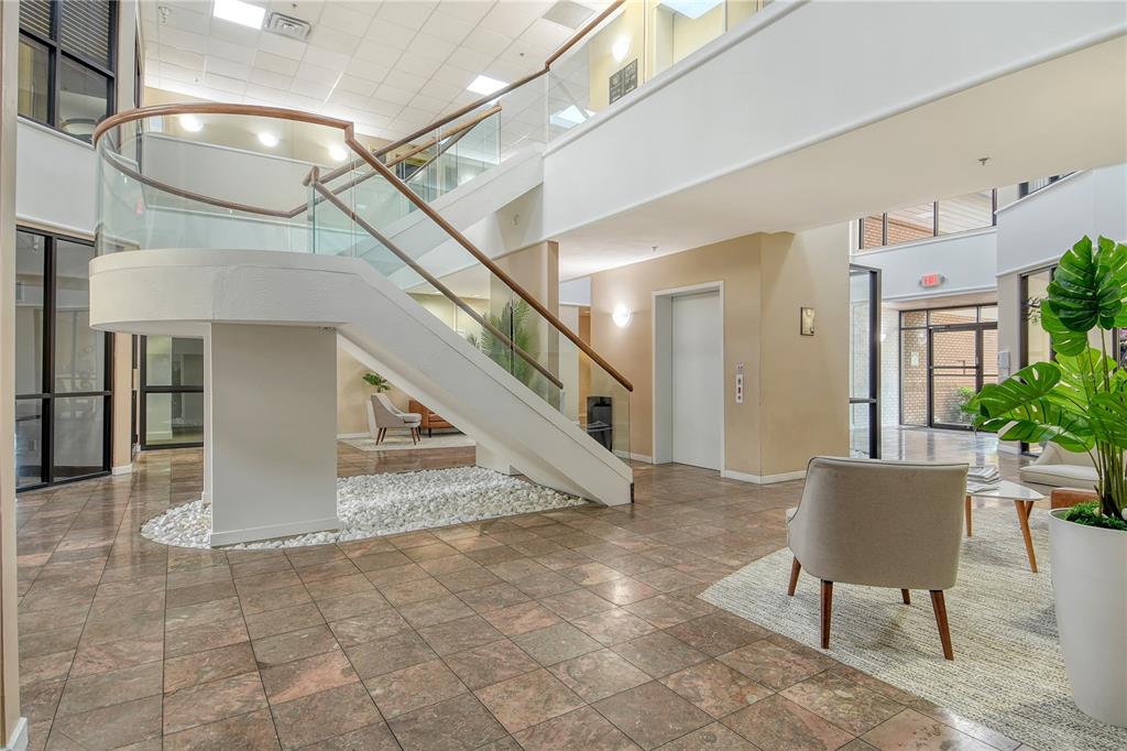 A modern office building lobby features a curved staircase, stone tile flooring, and seating areas — 3639 CORTEZ ROAD W UNIT 225, BRADENTON, FL