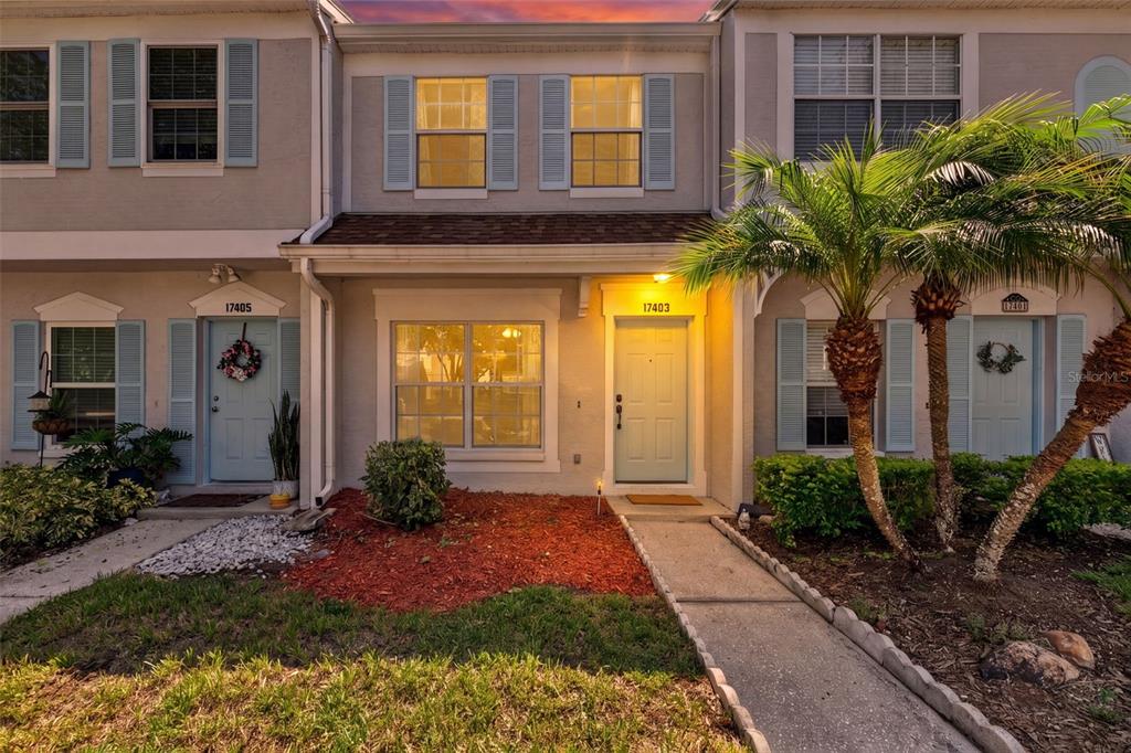 The exterior of a multi-unit townhouse features light-colored stucco walls, blue shutters, and palm trees — 17403 FLATWOODS KEY DRIVE, TAMPA, FL