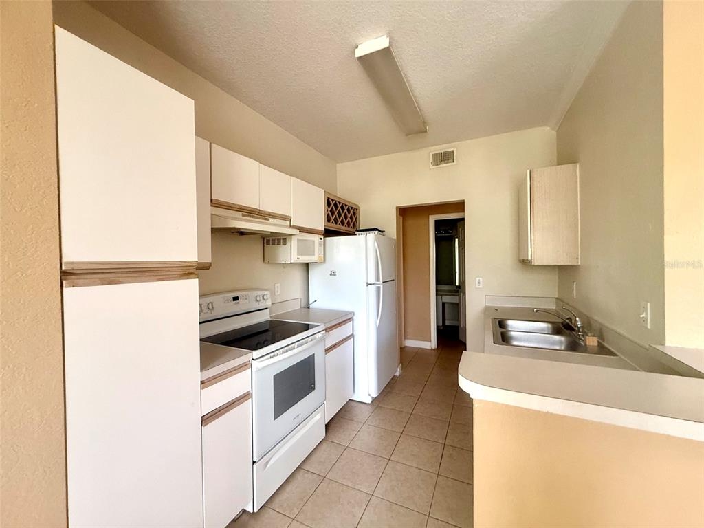 A kitchen features white cabinets, white appliances, tile flooring, and a double-basin stainless steel sink — 2668 ROBERT TRENT JONES DRIVE UNIT 434, ORLANDO, FL