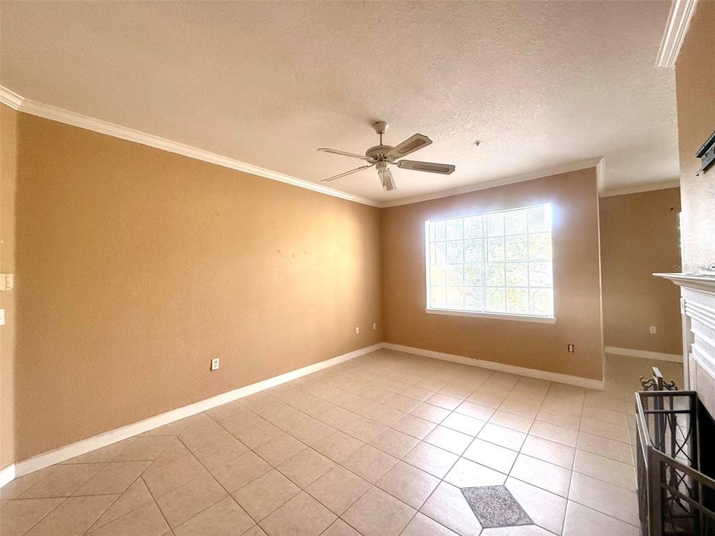 An empty living room features beige walls, tile flooring, a ceiling fan, and a fireplace — 2668 ROBERT TRENT JONES DRIVE UNIT 434, ORLANDO, FL