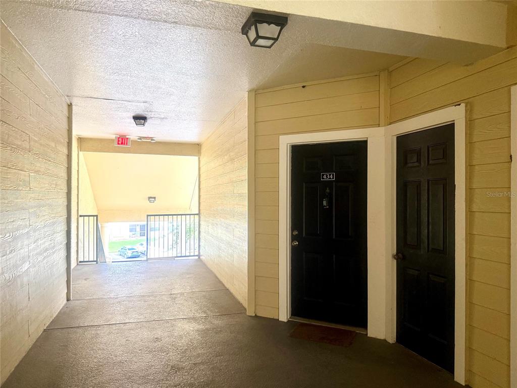 An outdoor apartment hallway features yellow siding, two black doors, and a metal railing — 2668 ROBERT TRENT JONES DRIVE UNIT 434, ORLANDO, FL