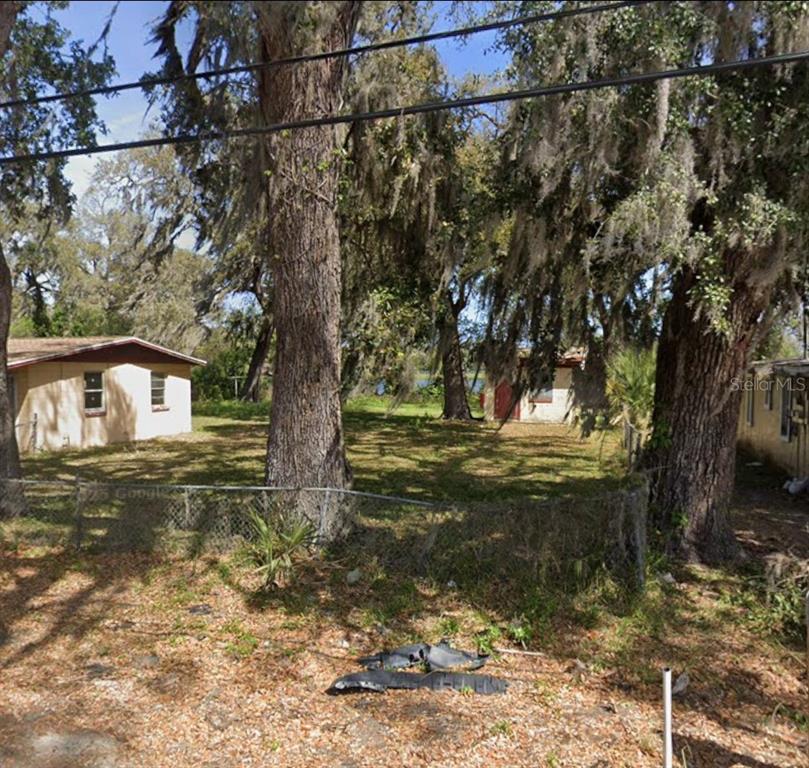 A grassy lot with large trees and two small buildings sits behind a chain-link fence — 529 FULTON STREET, DAYTONA BEACH, FL