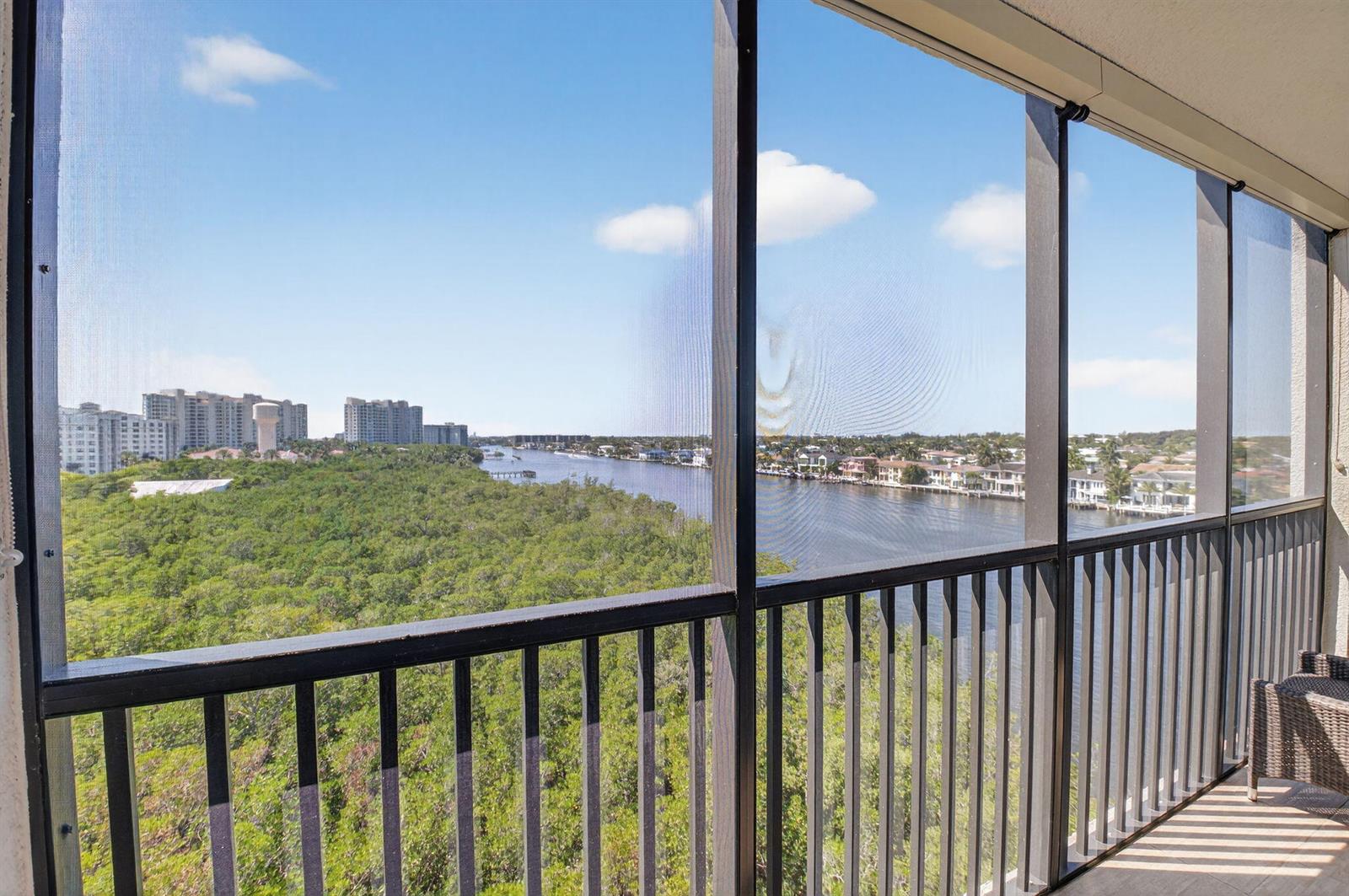 A screened-in balcony overlooks a waterway, dense green trees, and distant high-rise buildings — 3420 S Ocean Boulevard # 8z, Highland Beach FL 33487, HIGHLAND BEACH, FL