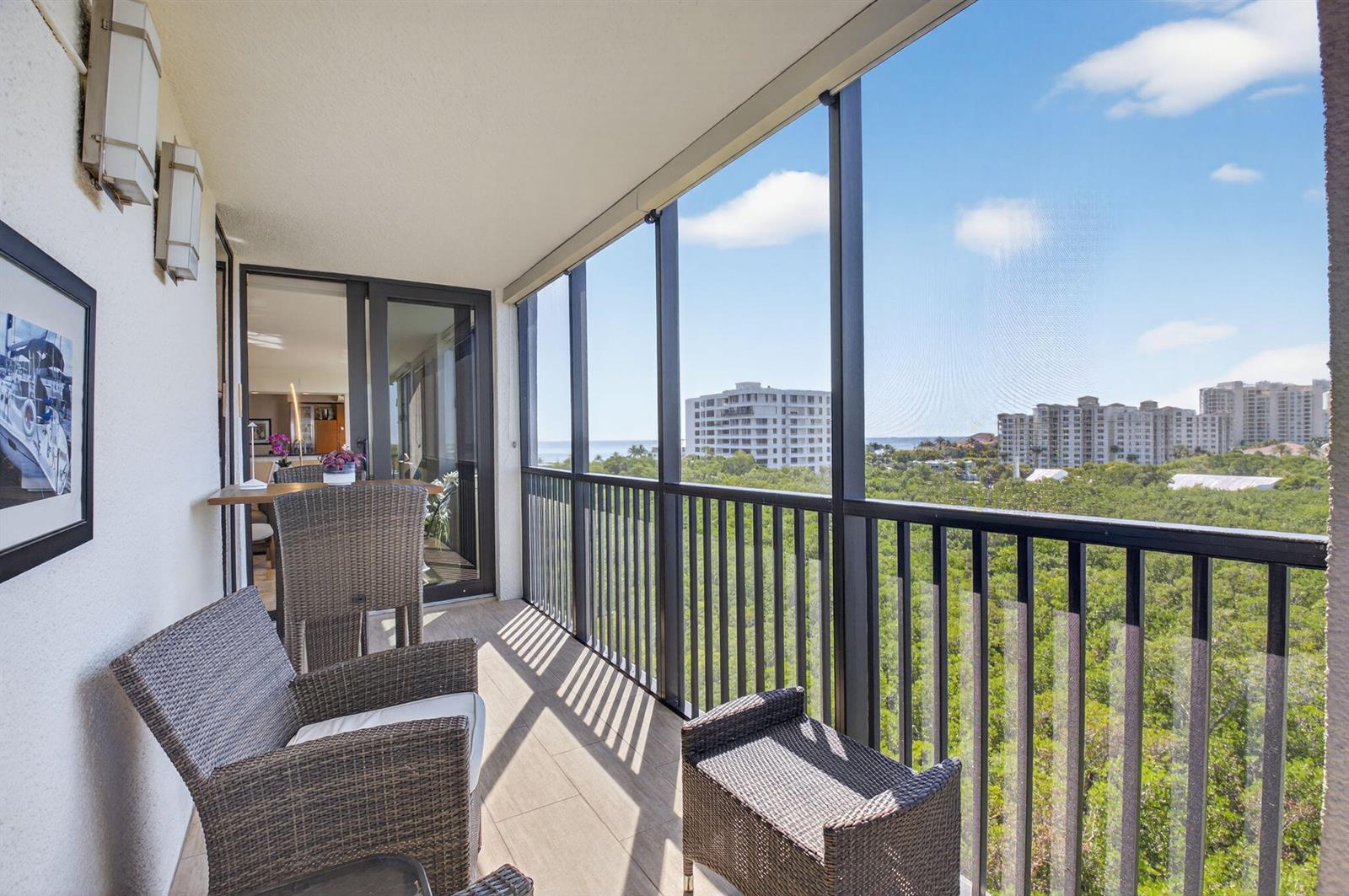 A screened-in balcony features wicker furniture, tile flooring, and views of trees and buildings — 3420 S Ocean Boulevard # 8z, Highland Beach FL 33487, HIGHLAND BEACH, FL