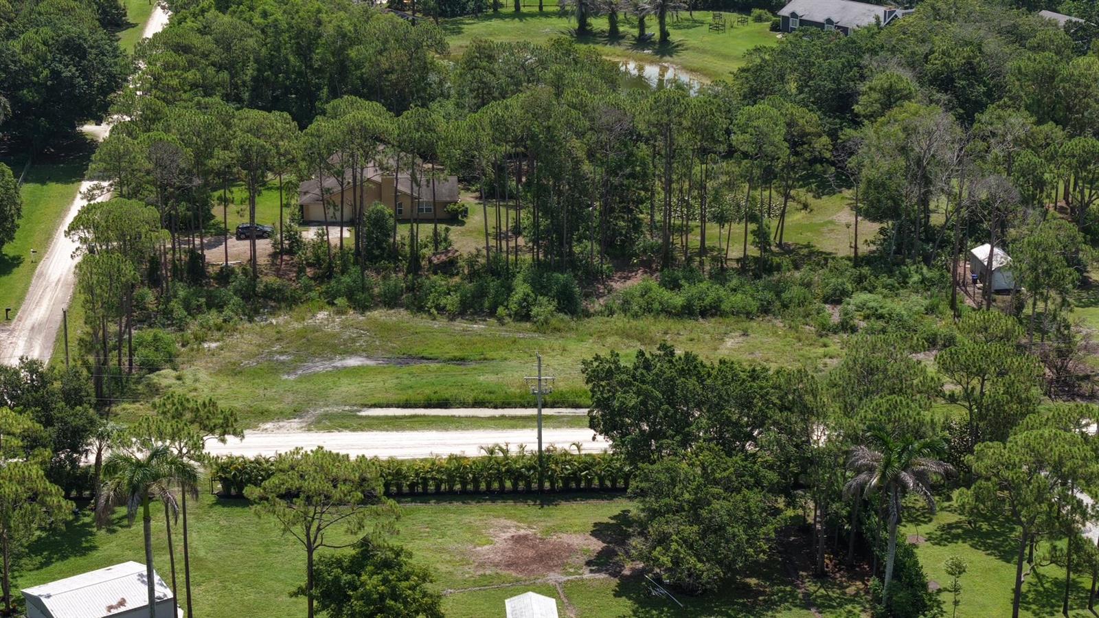 An aerial view shows a large, grassy lot with scattered trees and a gravel road — 0 129th Terrace N, FL 33478, FL