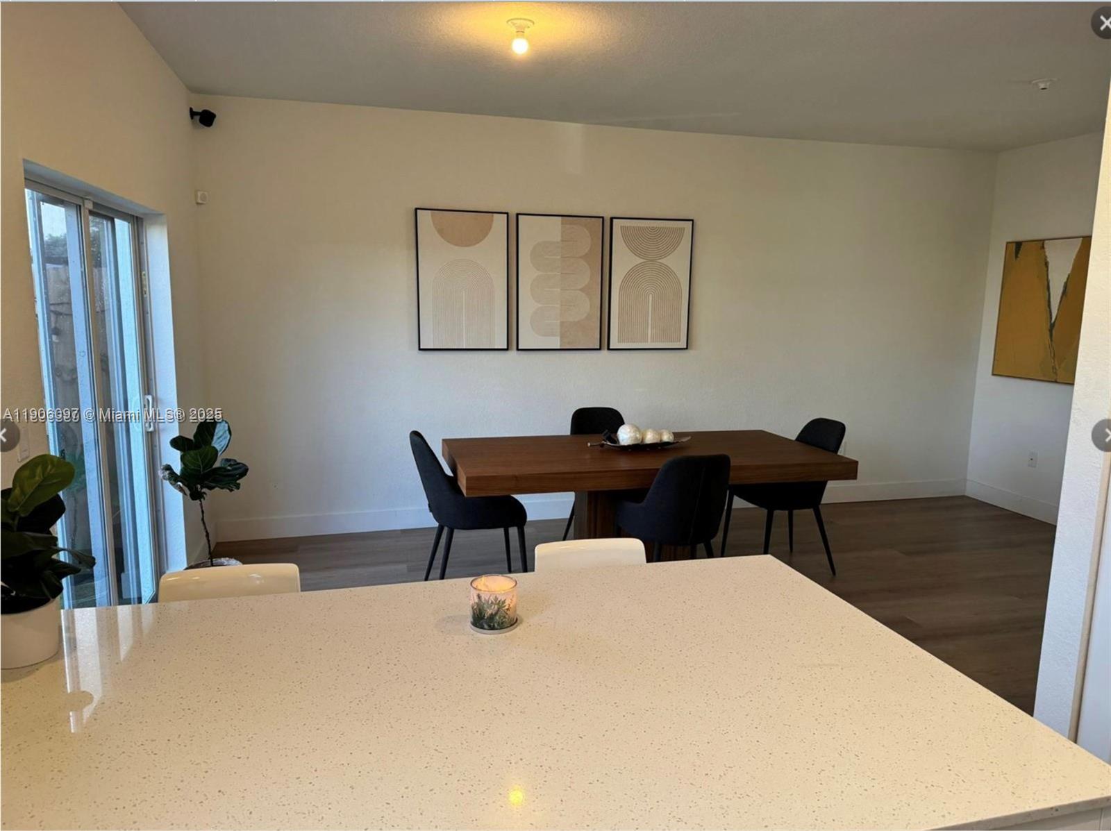 A dining area features a wooden table, dark chairs, and wall art near a kitchen island — 12277 NW 24th Pl, Miami FL 33167, MIAMI, FL