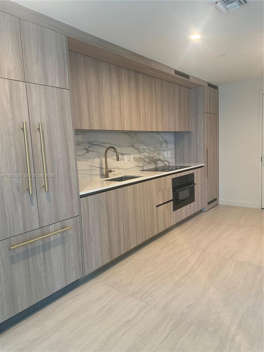 A modern kitchen features light wood cabinetry, a marble backsplash, and gold hardware — 77 SE 5th st # 2506, Miami FL 33131, MIAMI, FL