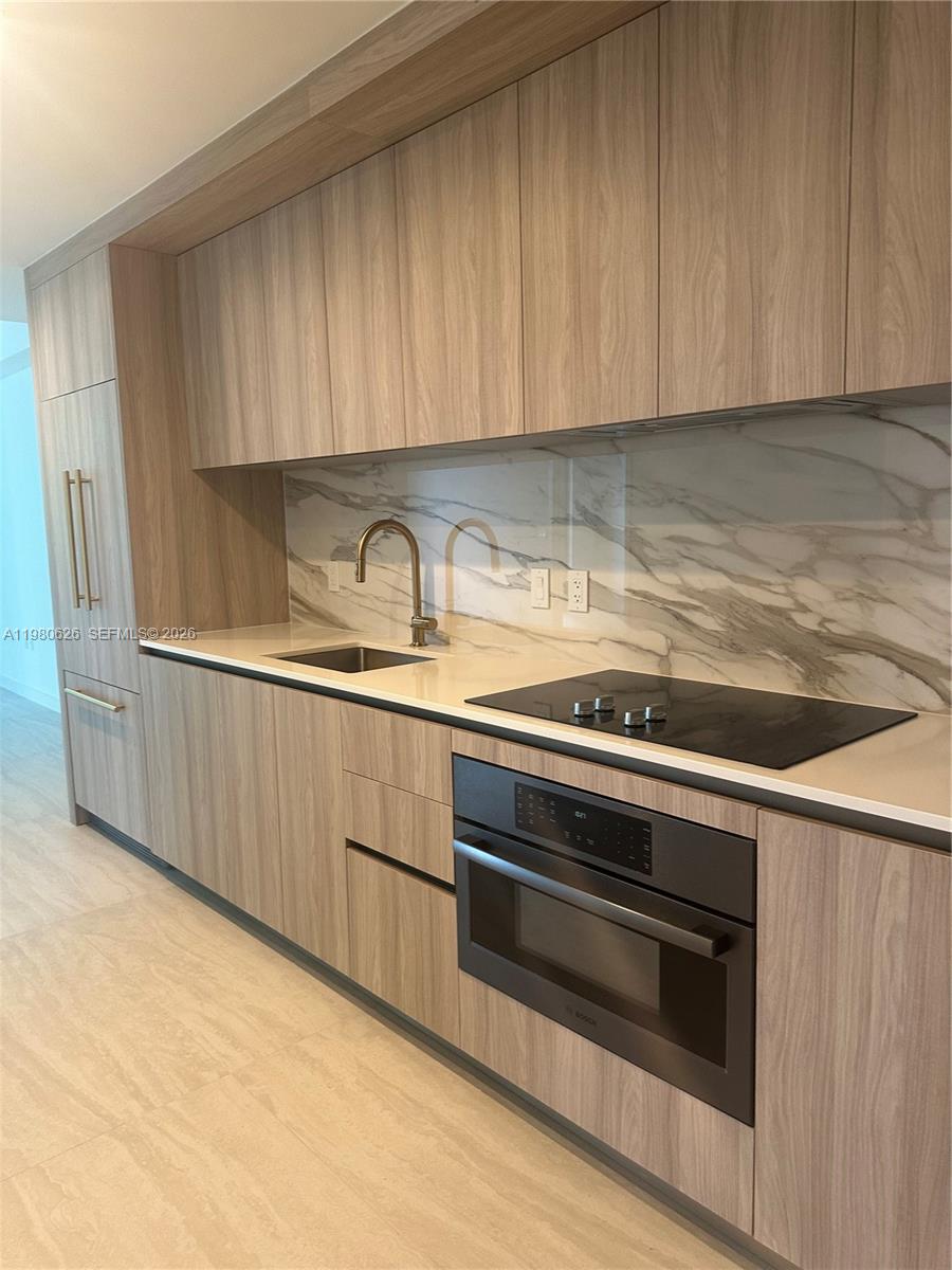 A modern kitchen features light wood cabinetry, a marble backsplash, and stainless steel appliances — 77 SE 5th st # 2506, Miami FL 33131, MIAMI, FL