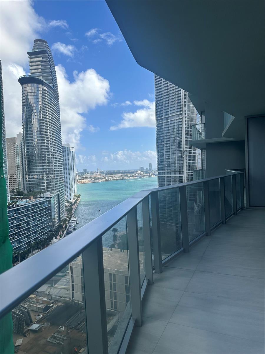 A high-rise balcony with a glass railing overlooks a bay and city skyline — 77 SE 5th st # 2506, Miami FL 33131, MIAMI, FL