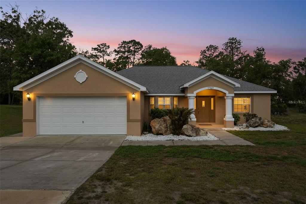 A single-story house with a two-car garage, tan stucco exterior, and a covered front porch — 17469 MABERLY ROAD, WEEKI WACHEE, FL
