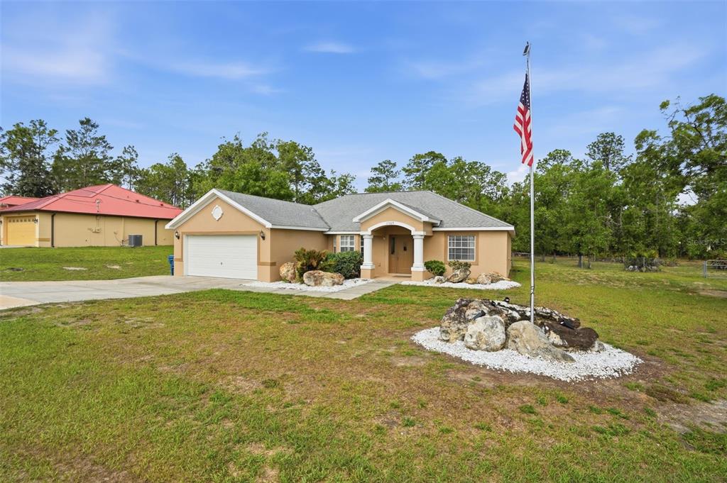A single-story tan house with a two-car garage and an American flag in the yard — 17469 MABERLY ROAD, WEEKI WACHEE, FL