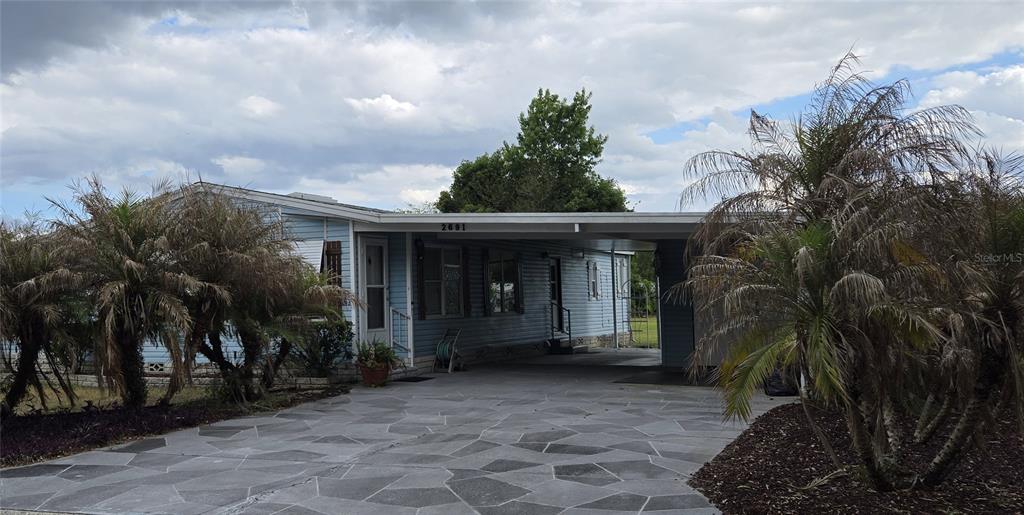 A light blue mobile home features a paved driveway, a carport, and surrounding palm trees — 2691 LAKE GRASSMERE CIRCLE UNIT 904, ZELLWOOD, FL