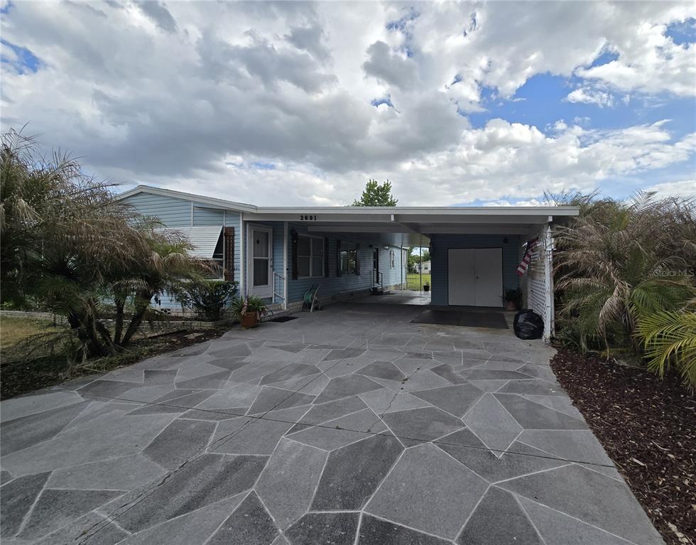 A light blue manufactured home features a large patterned concrete driveway and a covered carport — 2691 LAKE GRASSMERE CIRCLE UNIT 904, ZELLWOOD, FL