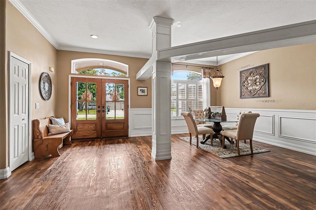 An entryway with wood floors leads to a dining area featuring a central support column — 663 SHERIDAN WOODS DR, MELBOURNE, FL