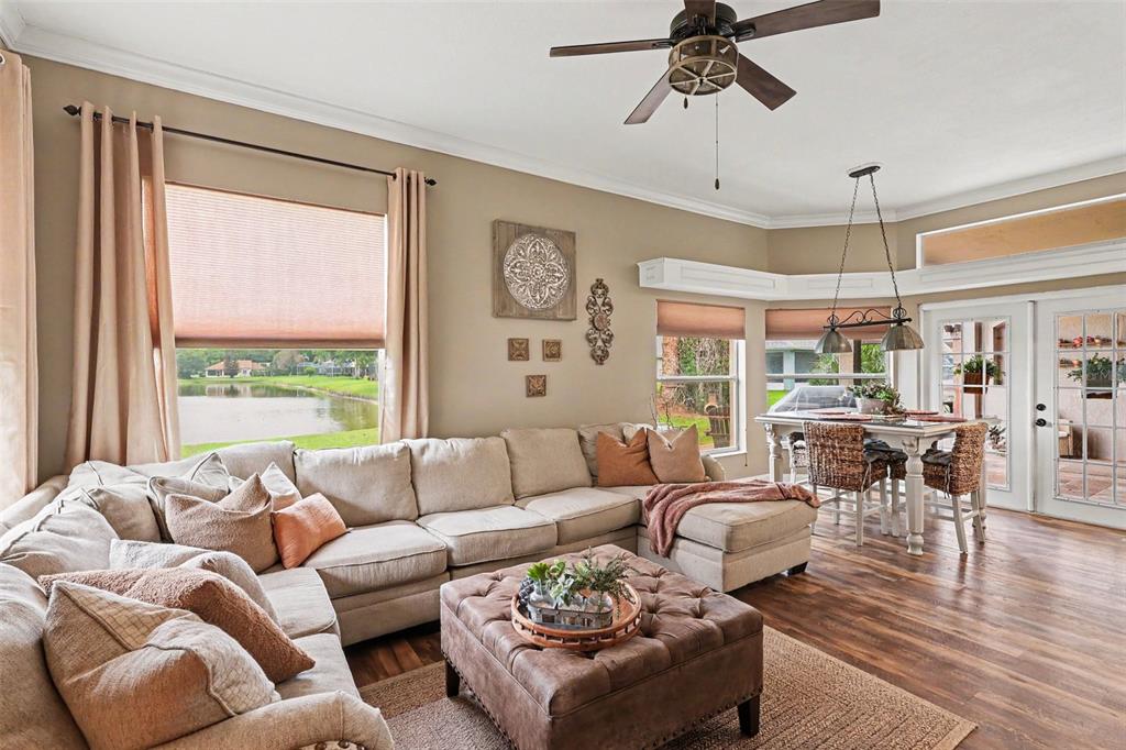 A living room with a sectional sofa, tufted ottoman, and dining area overlooking a lake — 663 SHERIDAN WOODS DR, MELBOURNE, FL
