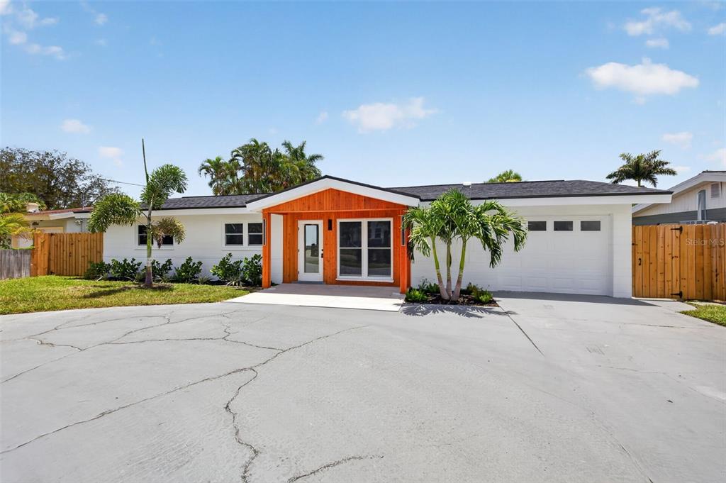 A single-story house with white siding, a wood-paneled entryway, and a cracked concrete driveway — 1524 CARSON CIRCLE NE, ST PETERSBURG, FL