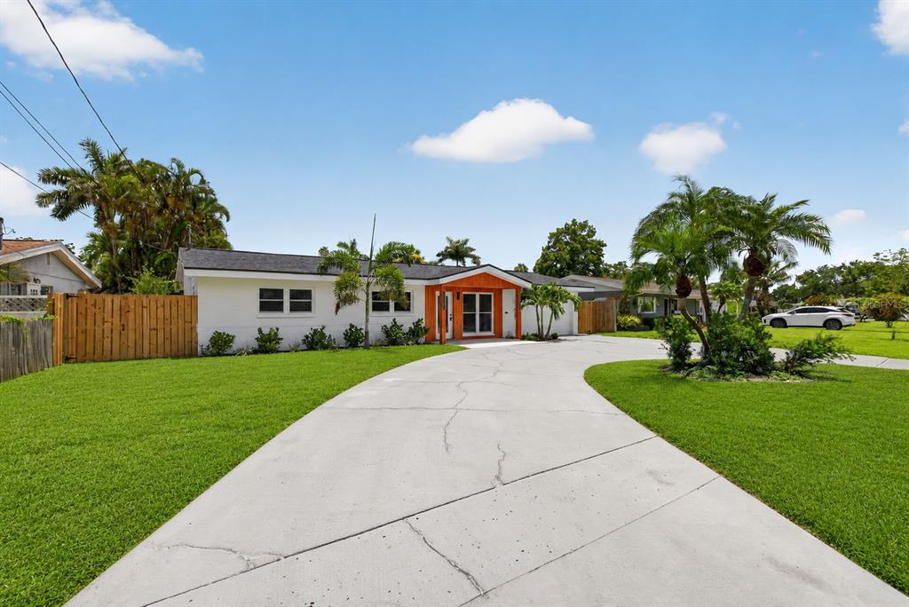 A white single-story house with a wood-accented entryway and a large concrete driveway — 1524 CARSON CIRCLE NE, ST PETERSBURG, FL