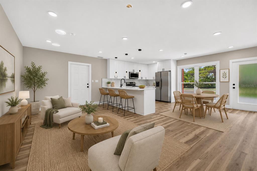 An open-concept living and dining area features white kitchen cabinets, a breakfast bar, and wood-look flooring — 1524 CARSON CIRCLE NE, ST PETERSBURG, FL