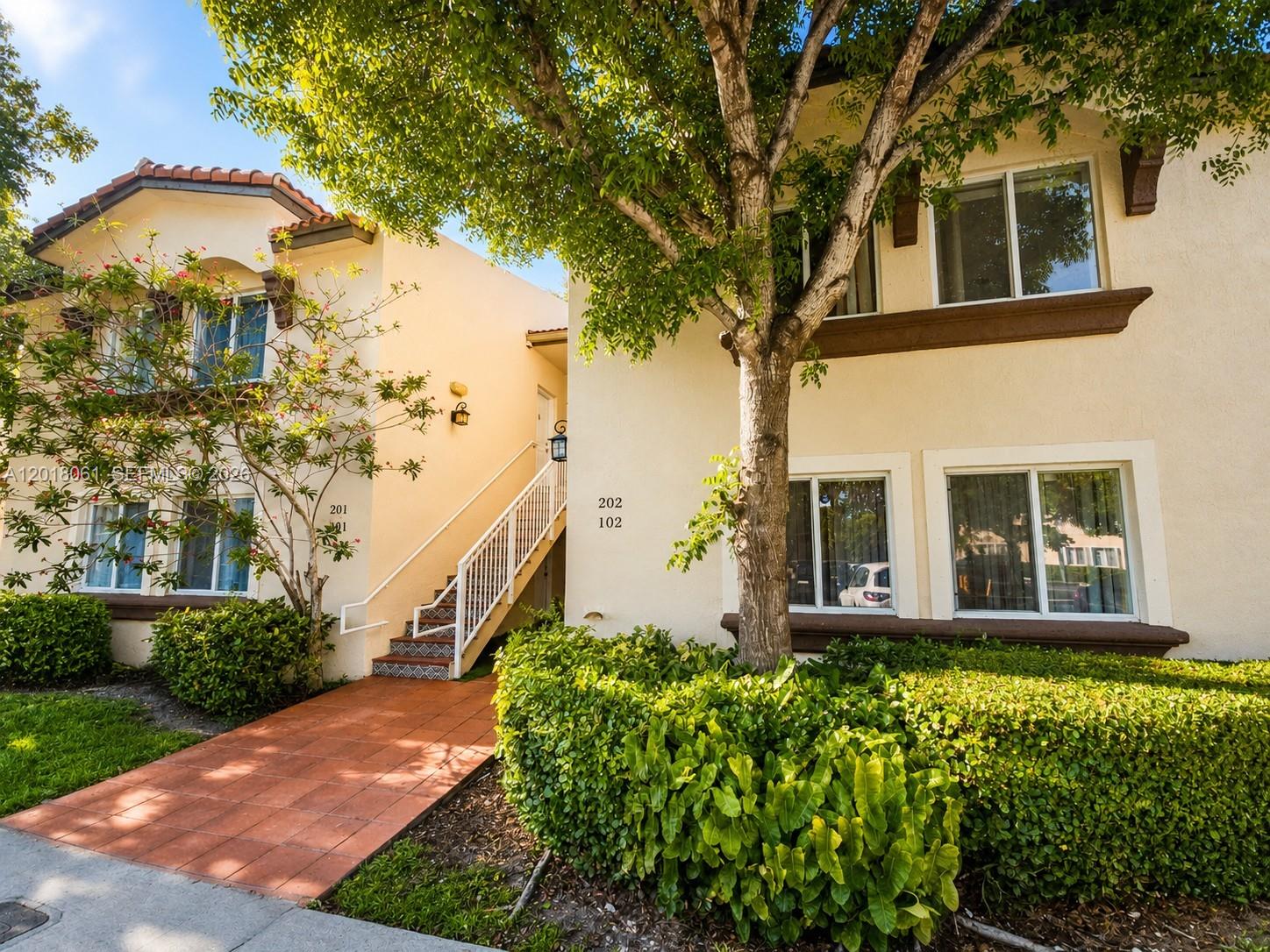 A two-story apartment building with beige stucco walls, a tiled walkway, and a large tree — 15721 SW 137th Ave # 202, Miami FL 33177, MIAMI, FL