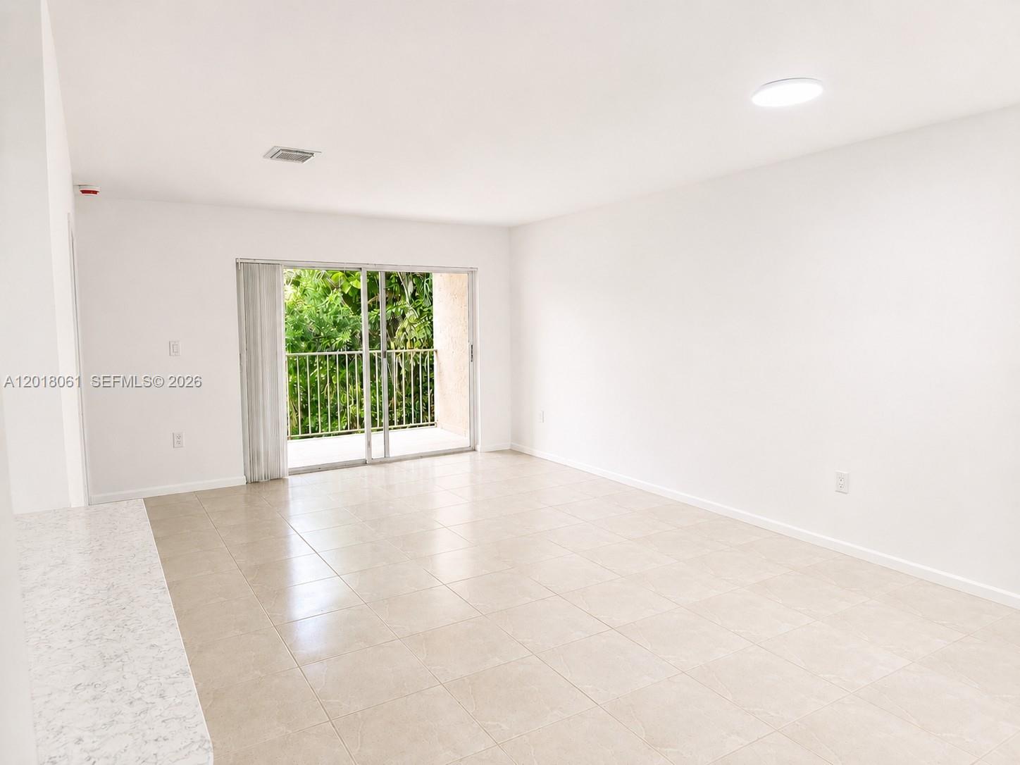 A bright, empty room features light-colored tile flooring, white walls, and a sliding glass door — 15721 SW 137th Ave # 202, Miami FL 33177, MIAMI, FL