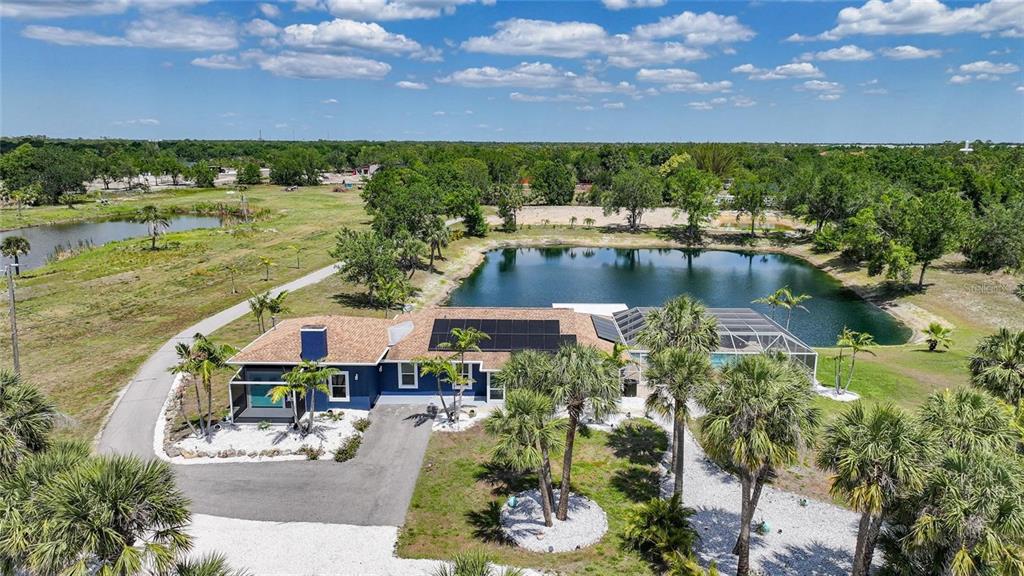 An aerial view of a blue house with solar panels and a pool by a pond — 24805 NOVA LANE, PUNTA GORDA, FL
