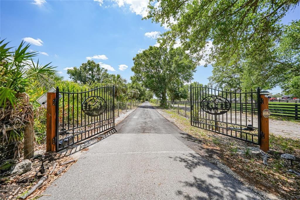 A paved driveway leads through an open decorative metal gate flanked by wooden posts — 24805 NOVA LANE, PUNTA GORDA, FL