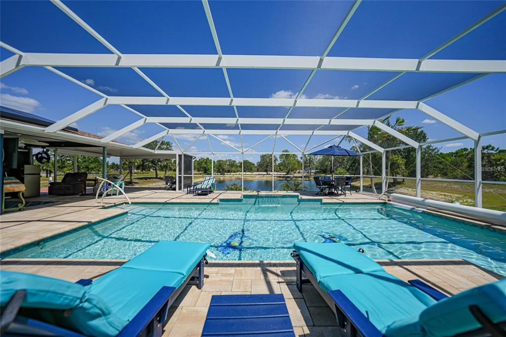 A screened-in pool patio features lounge chairs, a dining set, and a view of water — 24805 NOVA LANE, PUNTA GORDA, FL