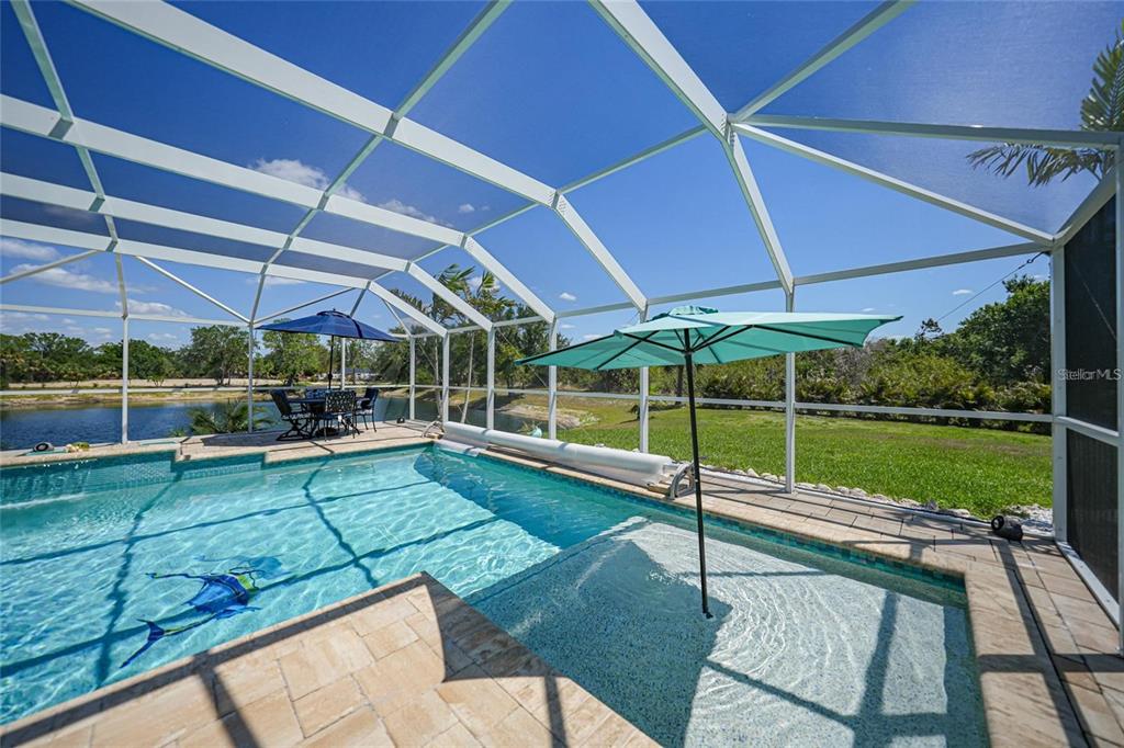 A screened-in swimming pool with a spa and patio furniture overlooks a lake — 24805 NOVA LANE, PUNTA GORDA, FL